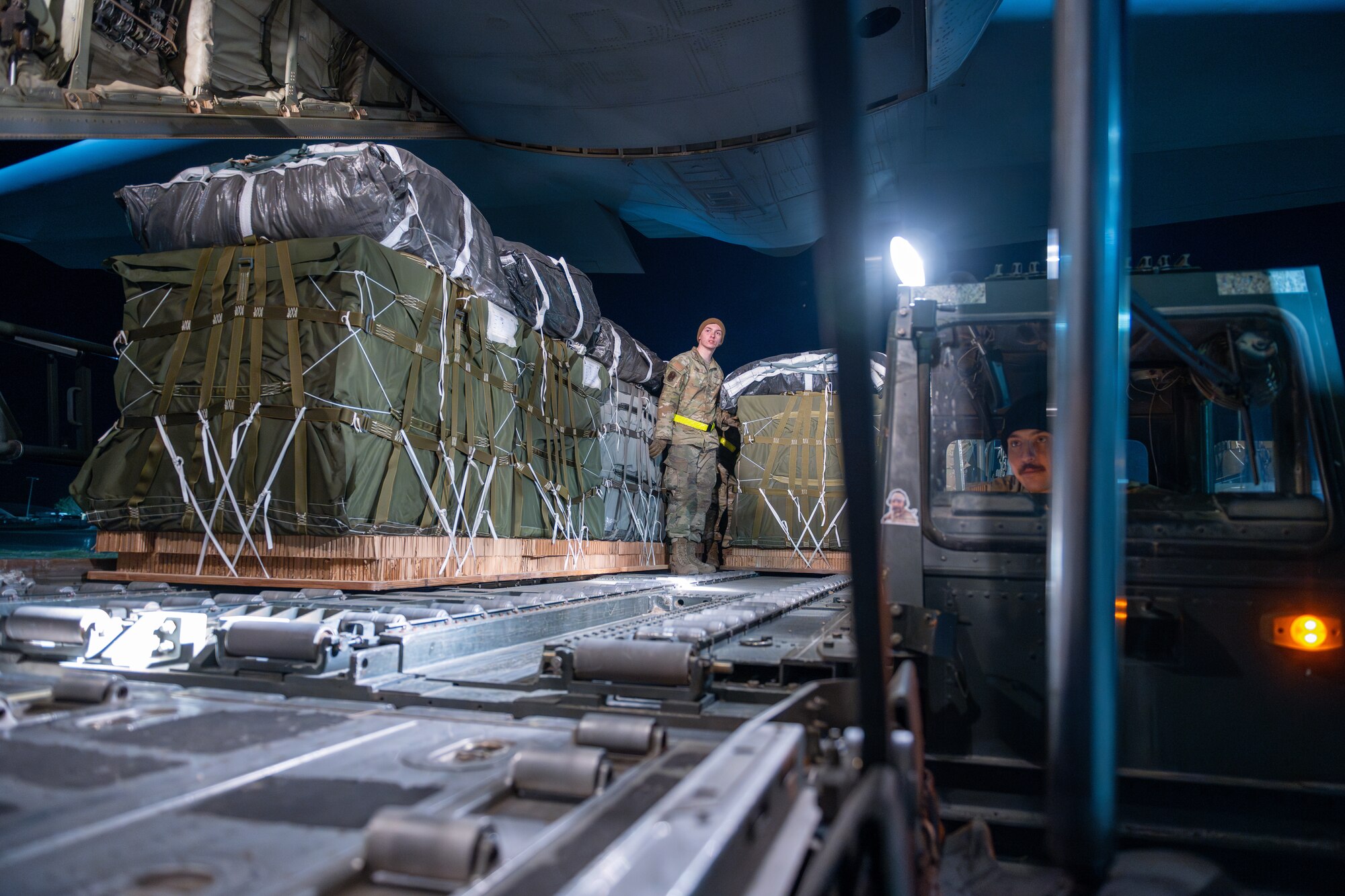 Airmen use a K-loader to move bundles of humanitarian air aboard a C-130J Super Hercules.