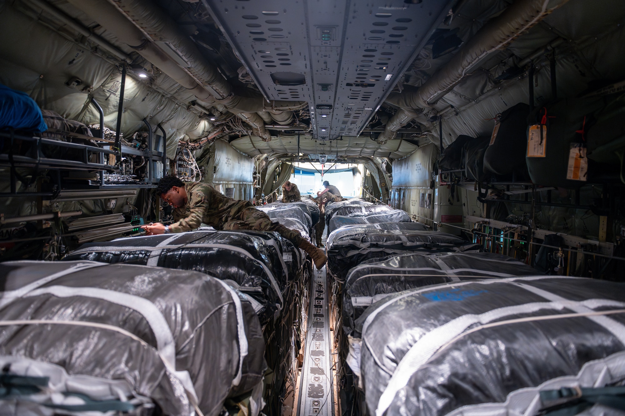 Loadmasters and parachute riggers aboard a C-130J Super Hercules inspect parachutes connected to pallets of humanitarian aid destined for Gaza.