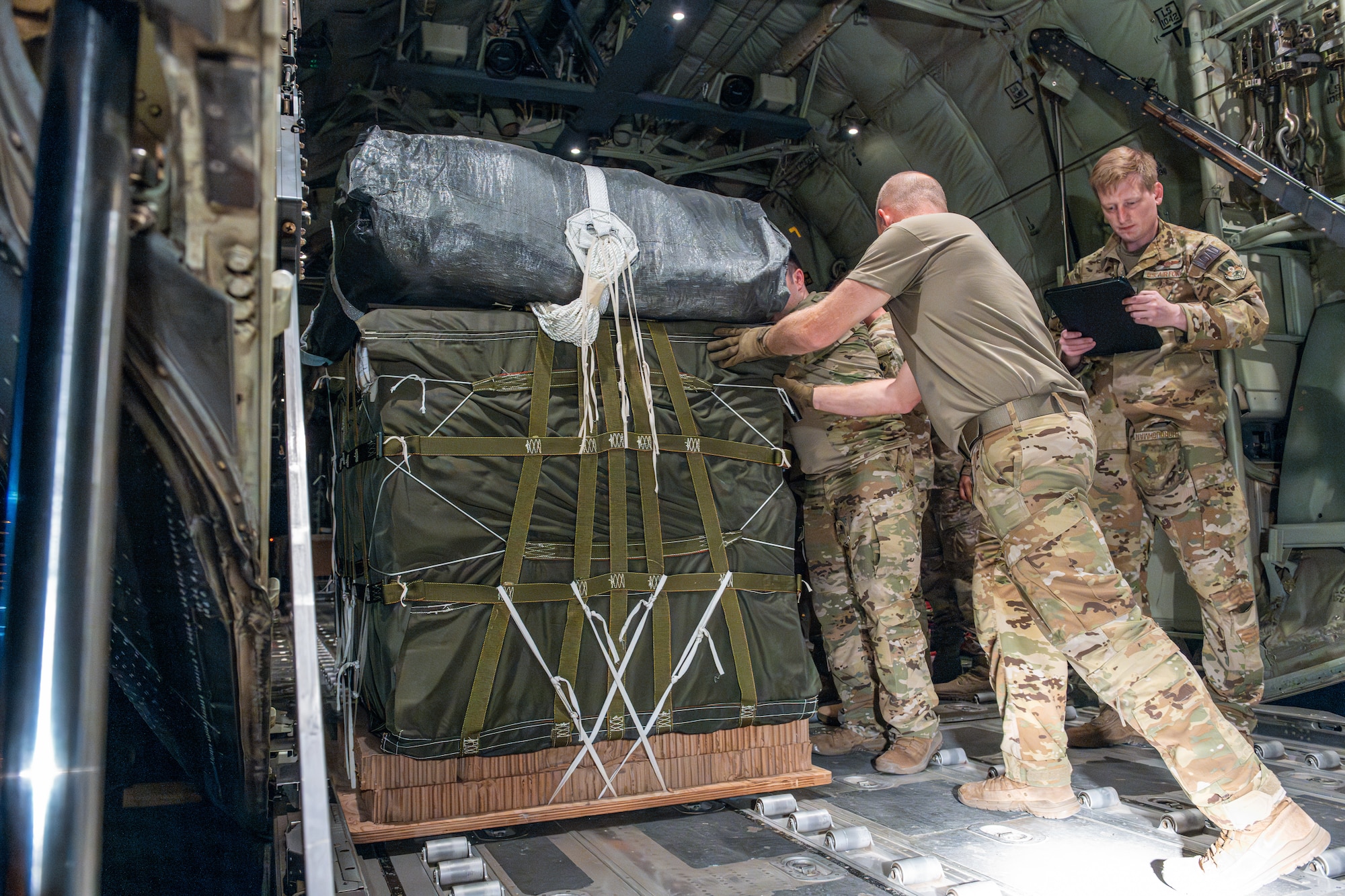 Airmen and Soldiers load pallets of humanitarian aid aboard a C-130J Super Hercules.