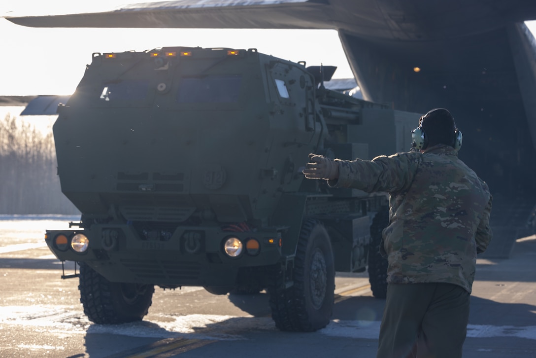 New York Air National Guard Tech. Sgt. Eric Junquera marshals a High Mobility Artillery Rocket System (HIMARS) off of a C-130 Hercules aircraft in support of Arctic Edge 24 at Eielson Air Force Base, Alaska, Feb. 24, 2024. Special Operations Command North deployed more than 400 joint and allied Special Operations Forces across the pan-Arctic region during Arctic Edge 24 to hone SOF’s ability to disrupt irregular and conventional threats, erode competitors’ confidence to hold the North American Arctic at risk, and employ layered defense of the Homeland. (U.S. Air National Guard photo by Tech. Sgt. Madison Scaringe)