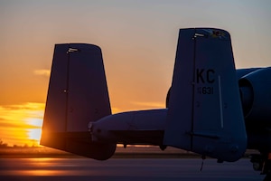 The sun sets behind the tail section of an A-10.