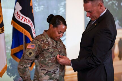 U.S. Army Brig. Gen. Robin Hoeflein, vice director of the Operations Directorate at the National Guard Bureau, looks on as her husband, Ray, affixes her rank to her uniform during a ceremony at Joint Base Myer-Henderson Hall, Virginia, where she was promoted to her current rank Feb. 29, 2024.