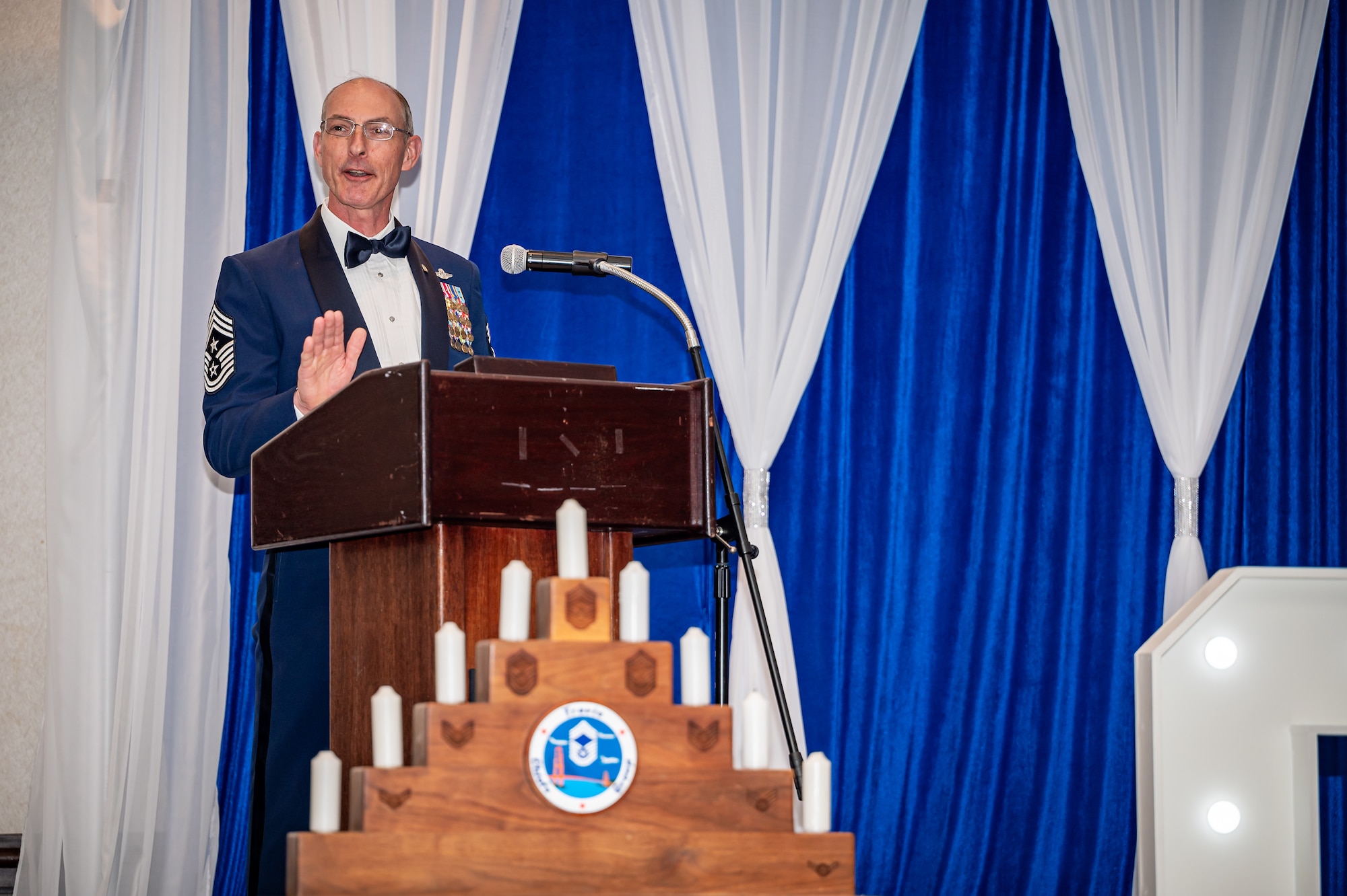 Retired Chief Master Sgt. Larry Williams gives a speech on stage behind a stepped candle holder representing the enlisted rank structure.