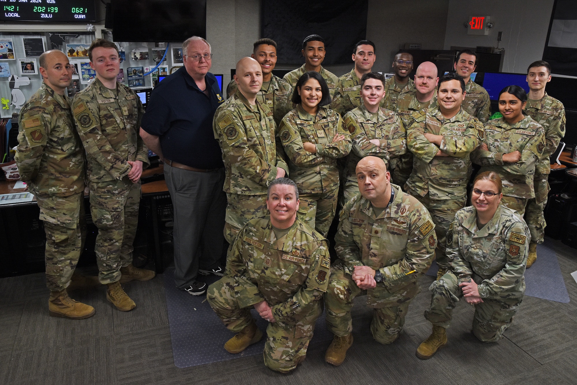 U.S. Air Force Airmen wearing OCP pattern uniforms pose for a photo in a dimly-lit command post. The room is filled with monitors and digital readouts.