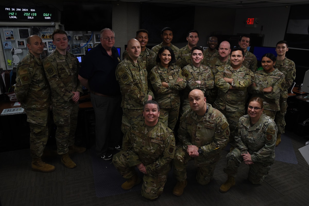 U.S. Air Force Airmen wearing OCP pattern uniforms pose for a photo in a dimly-lit command post. The room is filled with monitors and digital readouts.
