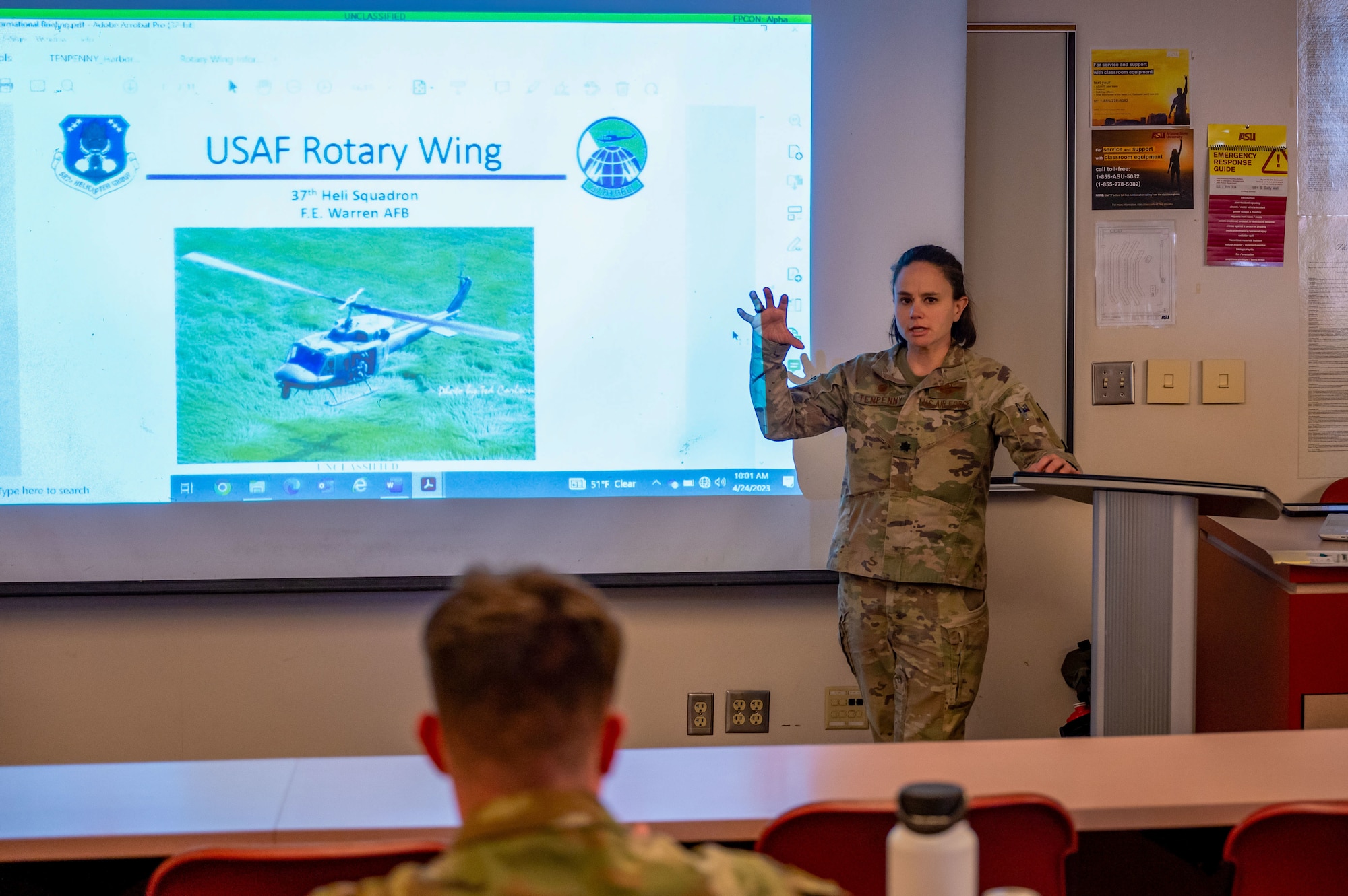 Lt. Col. Kathleen Tenpenny stands in front of a class presenting slides on the UH-1N Huey.