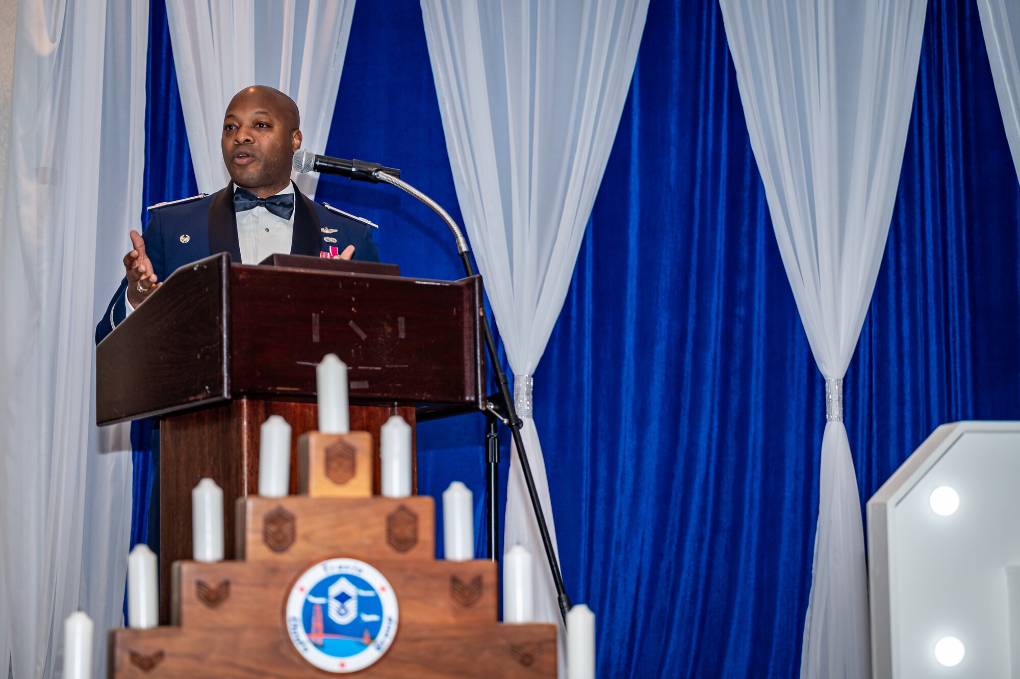 Col Brady-Lee gives a speech on stage behind a stepped candle holder representing the enlisted rank structure.