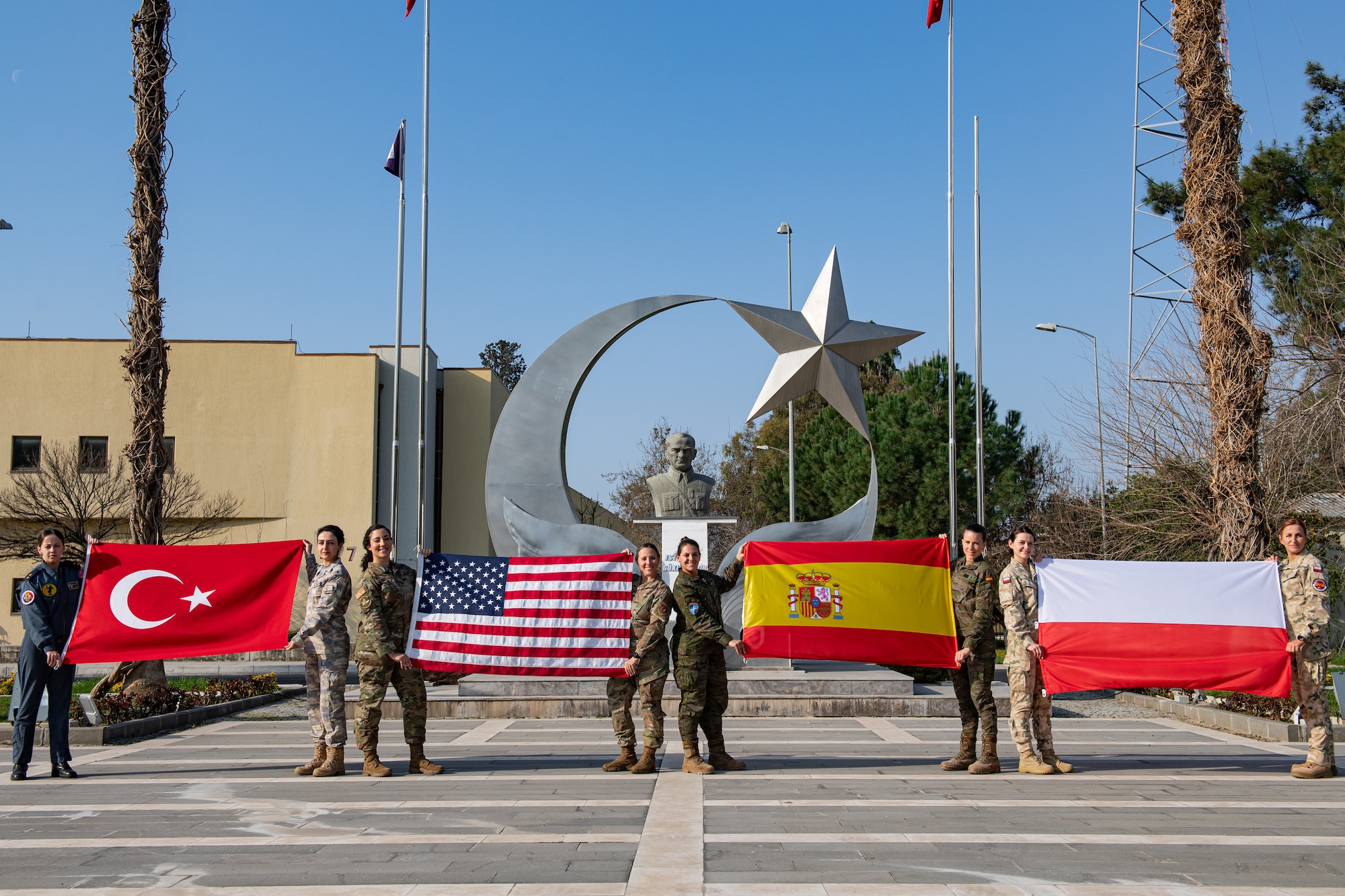 Female service members hold up corresponding country flags posing for photo
