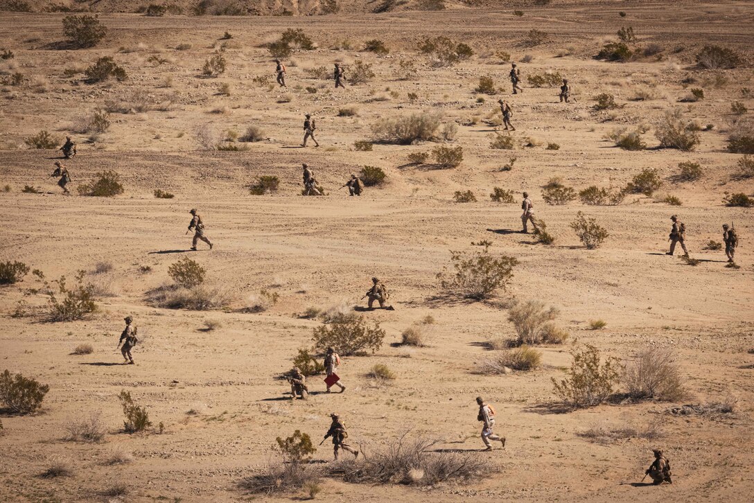 A group of Marines carrying weapons walk through a desert.