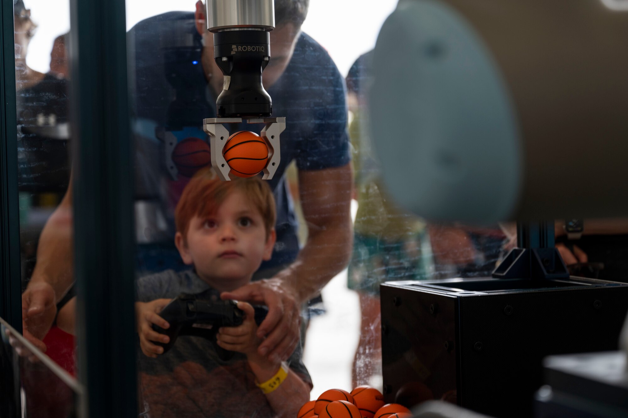 A boy uses a robotic controller to grab a mini basketball.