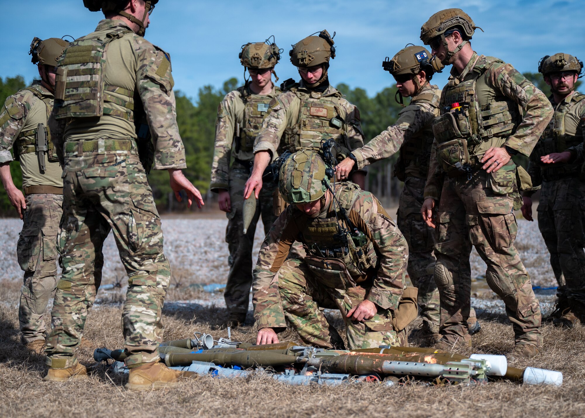 A group of men stand by a man kneeling over a training munition..