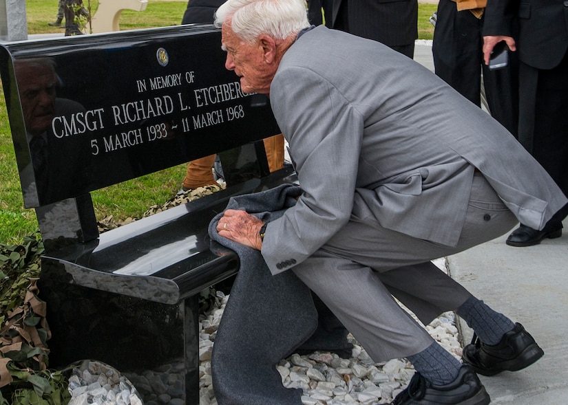 A man kneels in front of a bench with inscription on it.