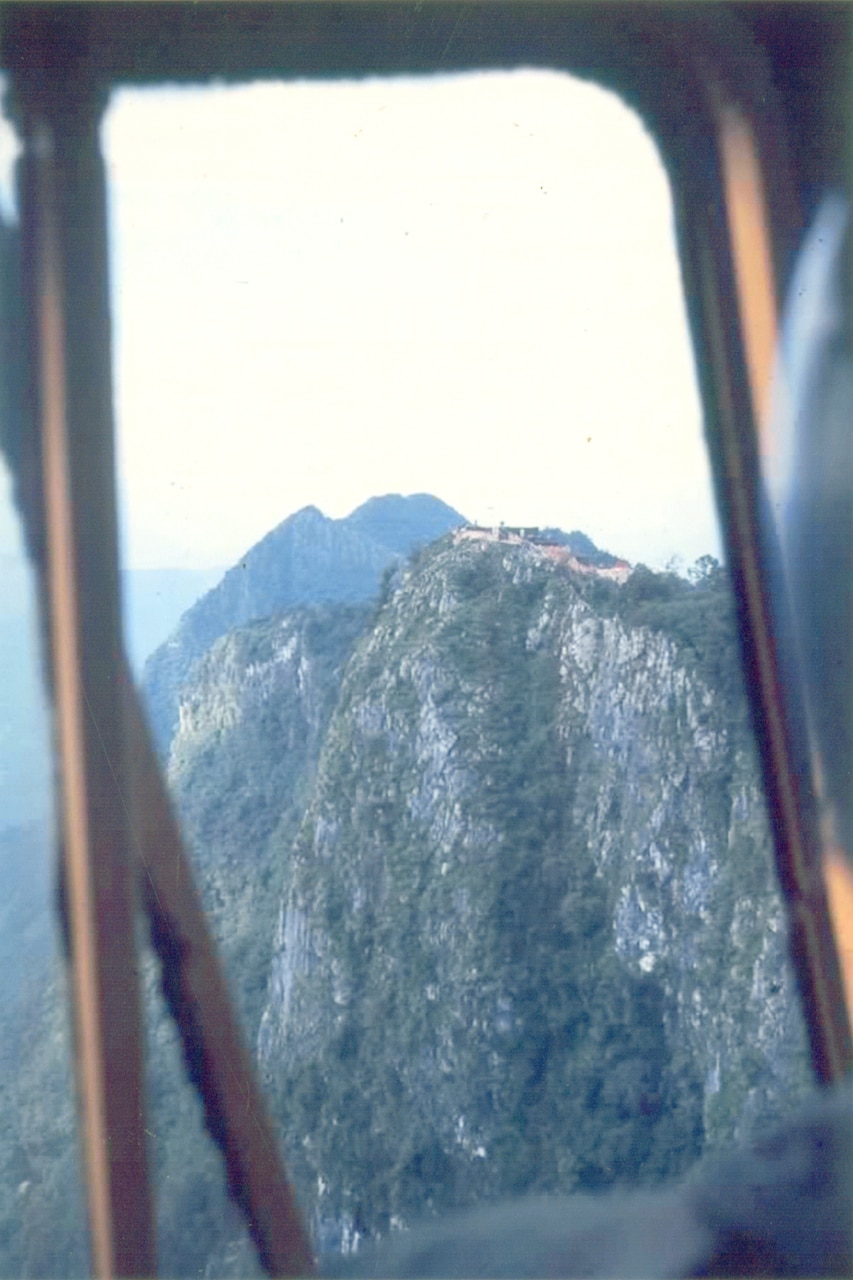 A tree-covered mountain is seen out of the window of an aircraft.