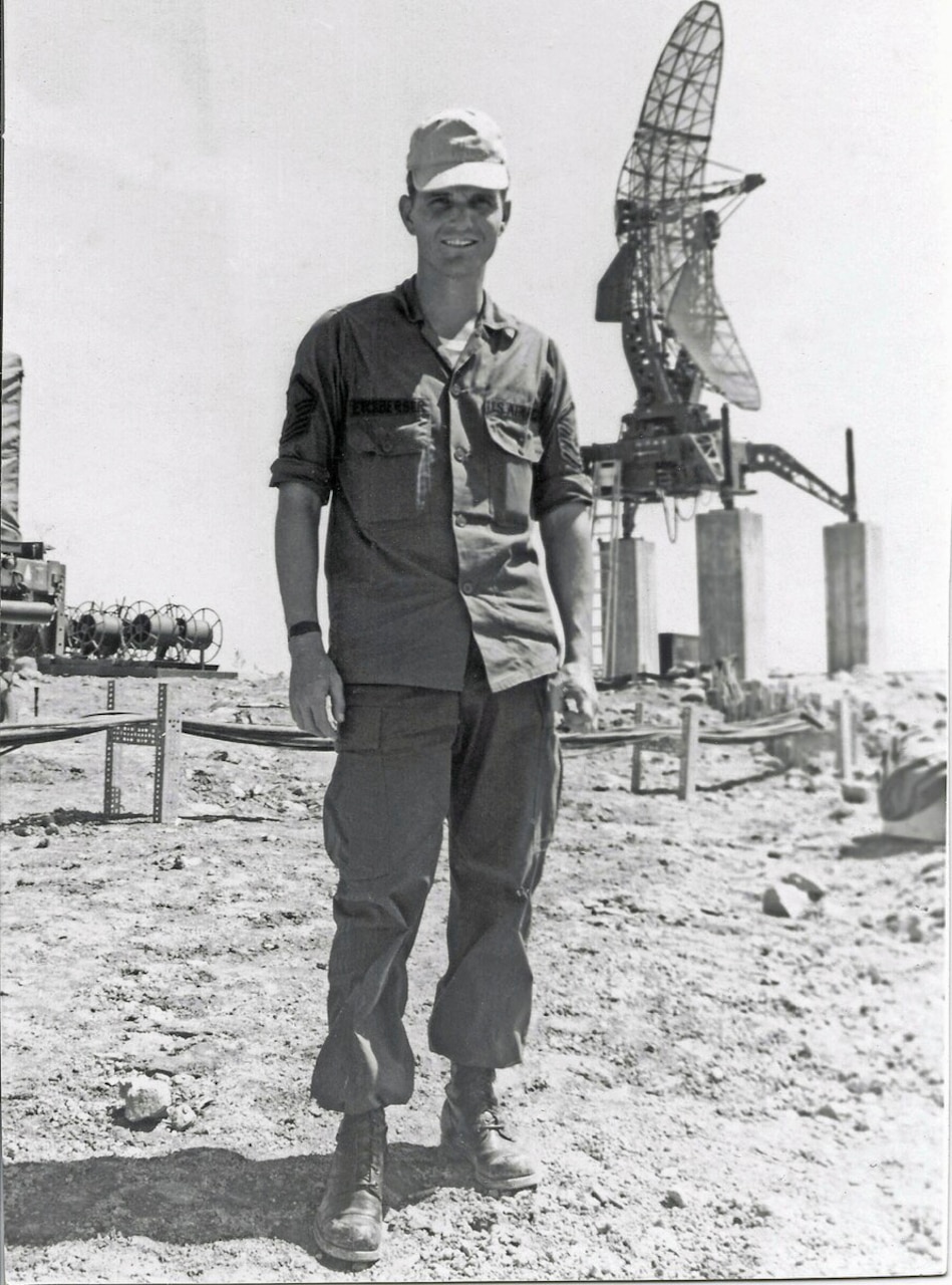 A smiling man poses for a photo in front of a large piece of radar equipment.