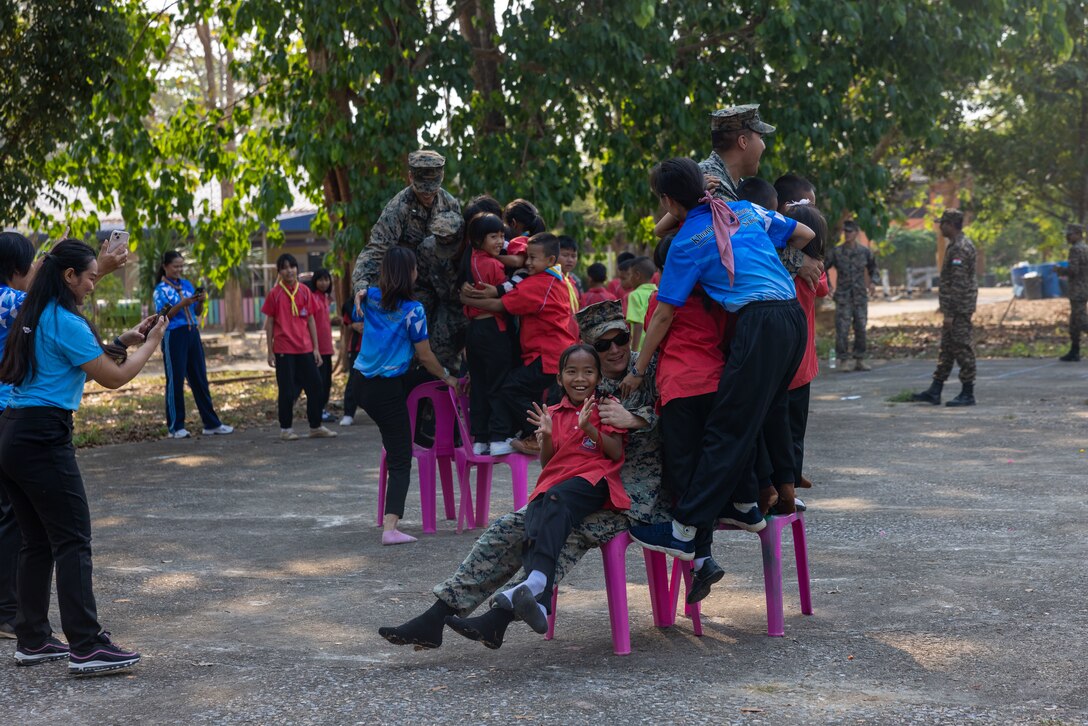 U.S. Marines with Marine Wing Support Squadron (MWSS) 174 and students from the Bankhaocha-Angkromklong School stand up on the chairs during a game of musical chairs at Rayong, Thailand, Feb. 15, 2024. Marines of MWSS-174 lent their engineering expertise to multilateral humanitarian efforts during Cobra Gold 24. Joint Exercise Cobra Gold is the largest joint exercise in mainland Asia and a concrete example of the strong alliance and strategic relationship between Thailand and the United States. This year will be the 43rd iteration of the multilateral exercise and will be held from Feb. 27 to March 8, 2024. (U.S. Marine Corps Photo by Cpl. Calah Thompson)