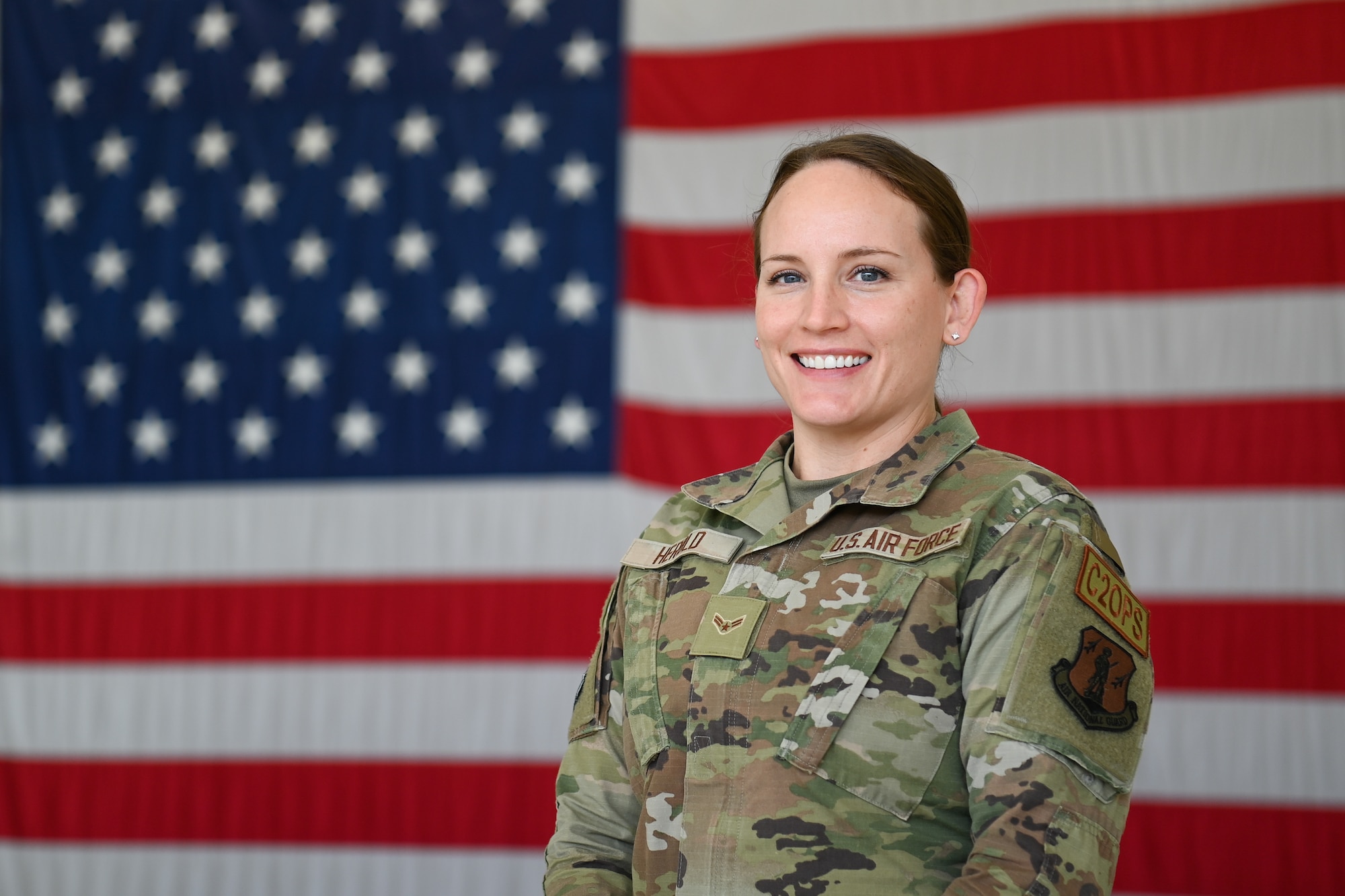 Female Airman in uniform stands for photo with large American flag in background.