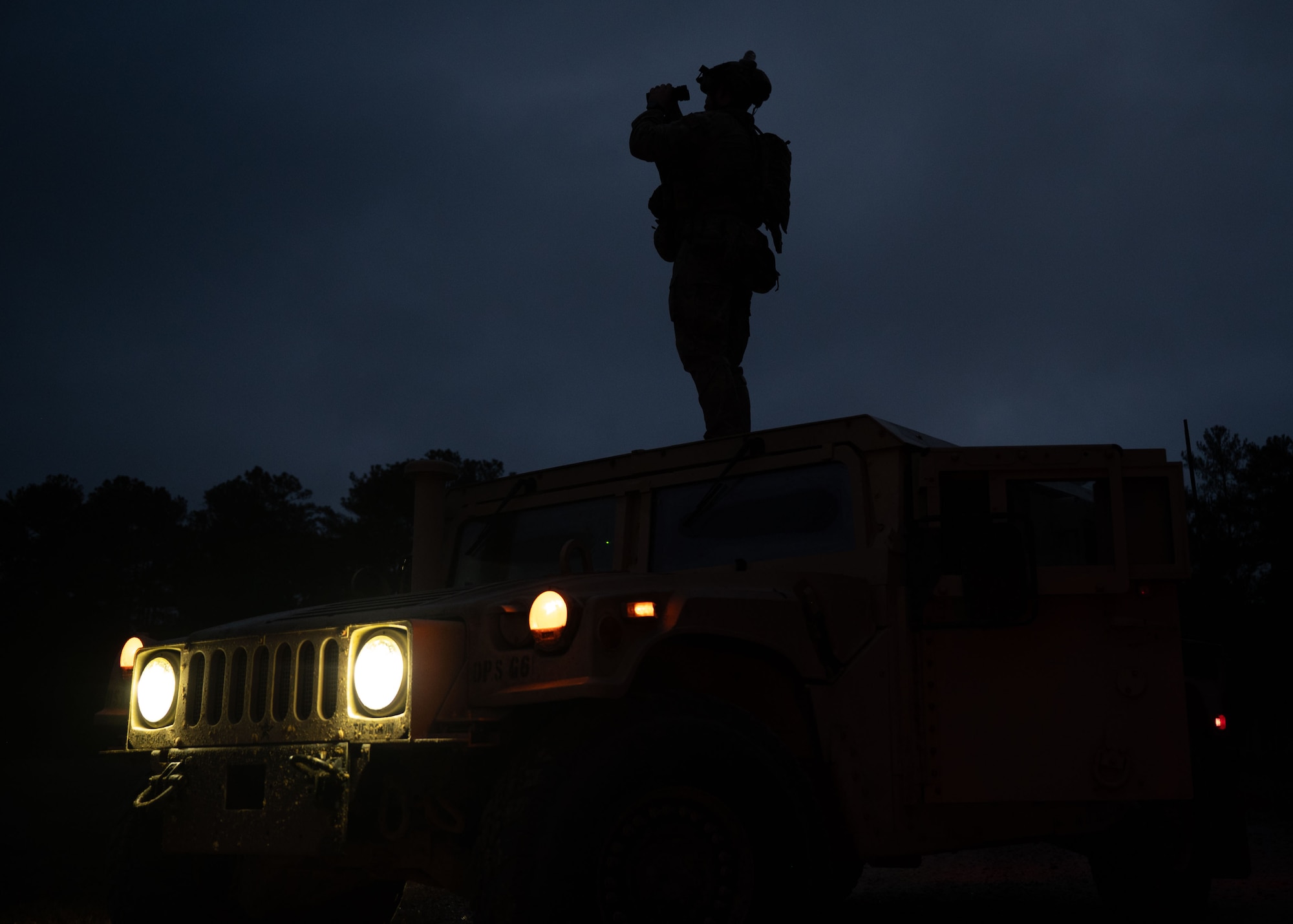 A man stands on the roof of a hummer with binoculars in the dark early morning hours.