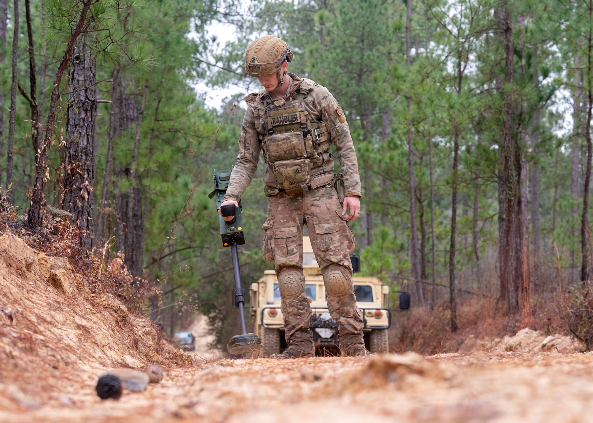 A man holds an EOD Minehound device to scan over the ground.