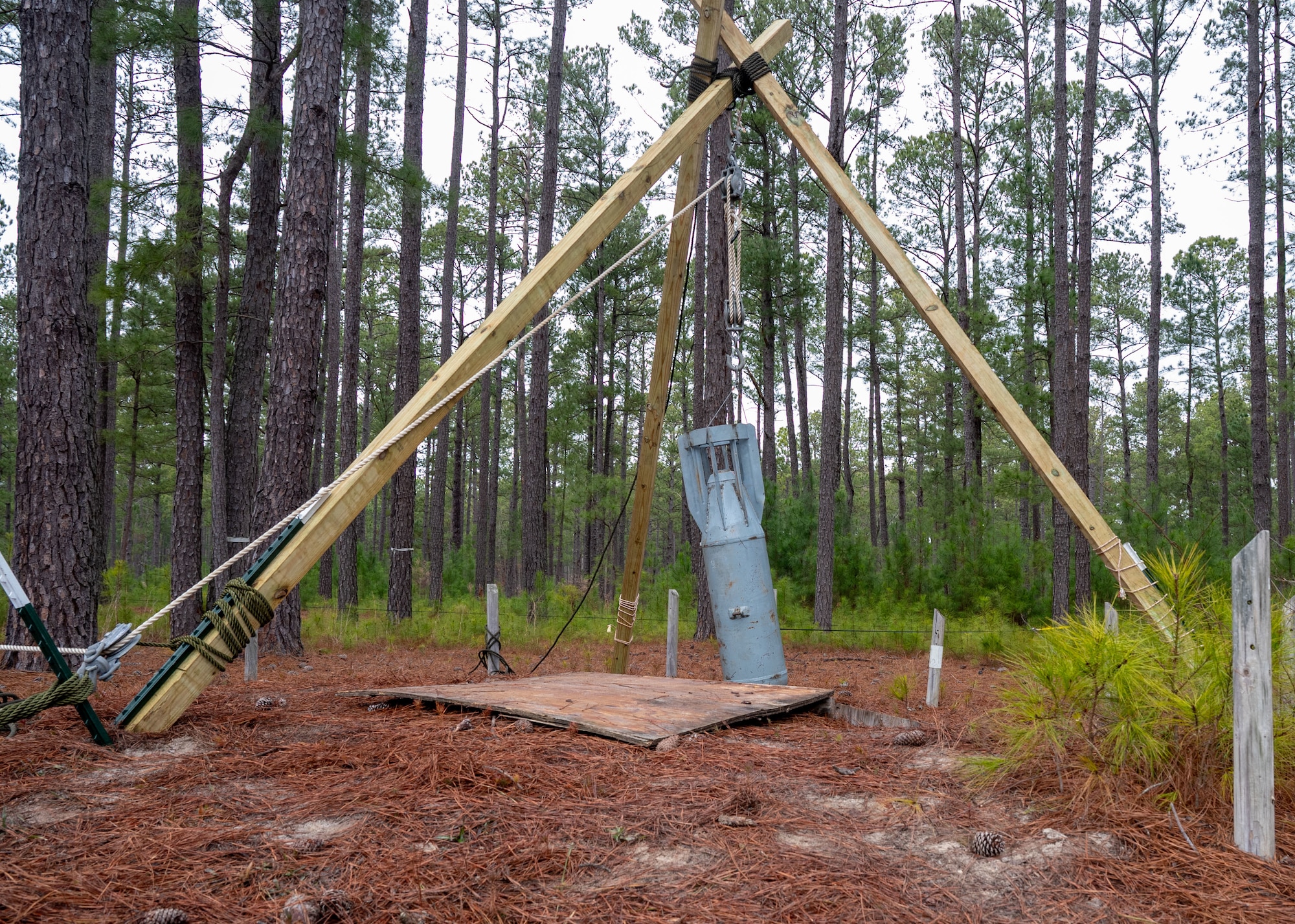 A wooden scaffold with a pulley hoists a training munition out of a hole.