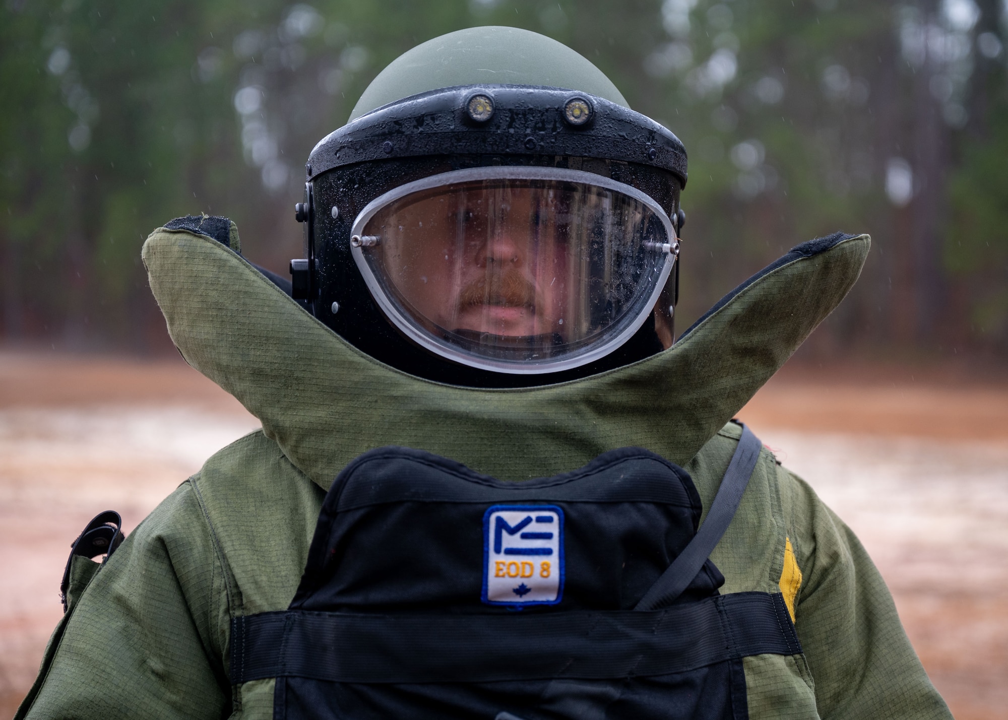 A man in an EOD protective bomb suit stands in a field.