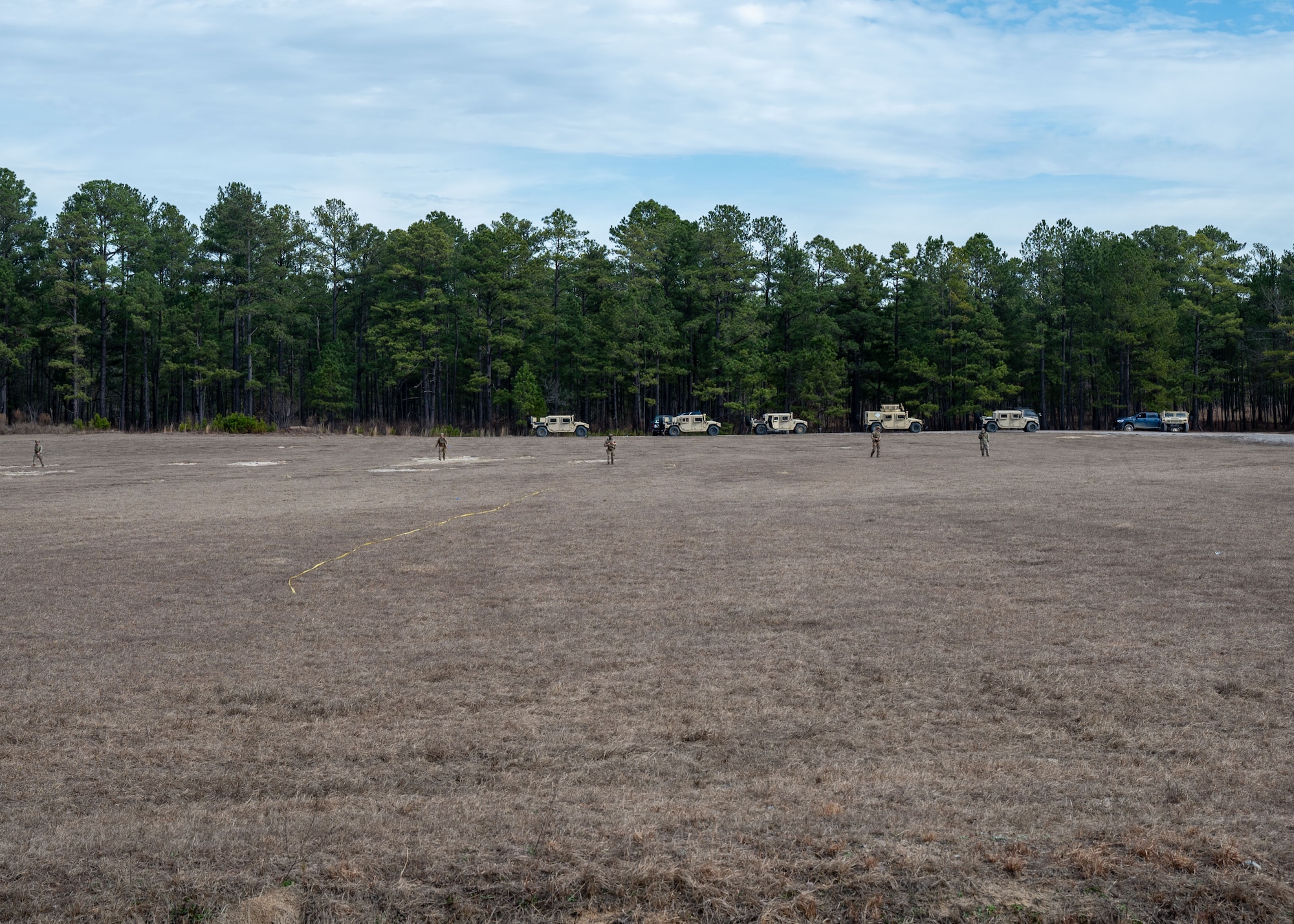 A wide shot of a field with hummers in the background and men spread out walking towards the camera.