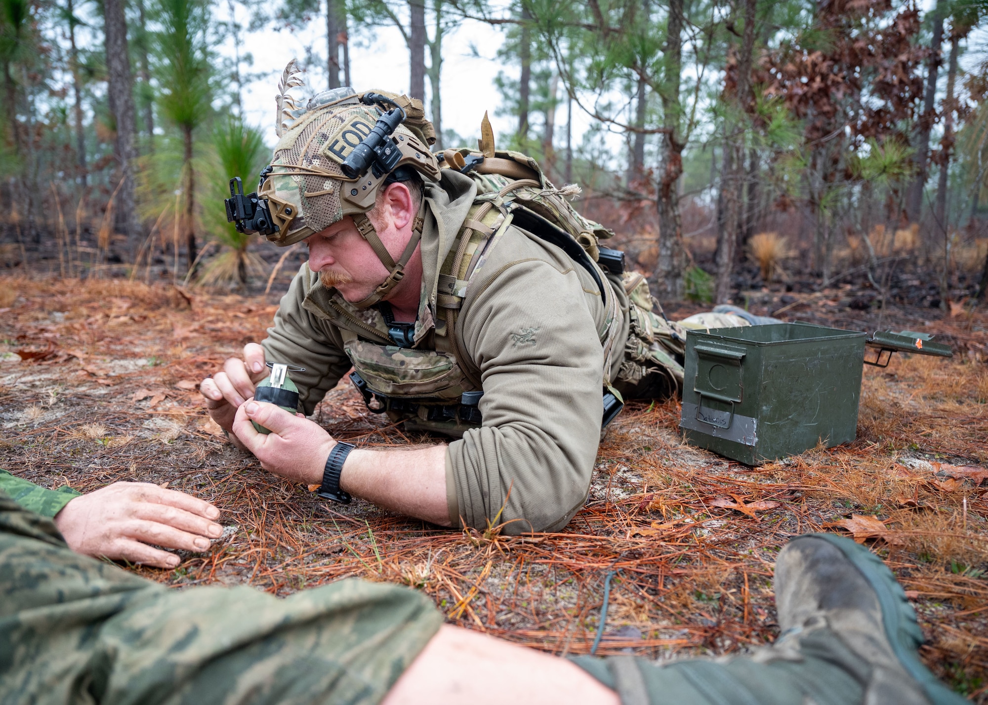 A man lies on the ground holding a training munition near a training mannequin.