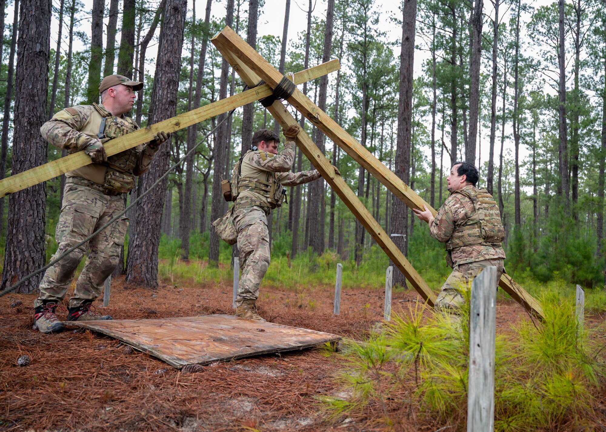 Thee men raise a wooden scaffold over a hole.