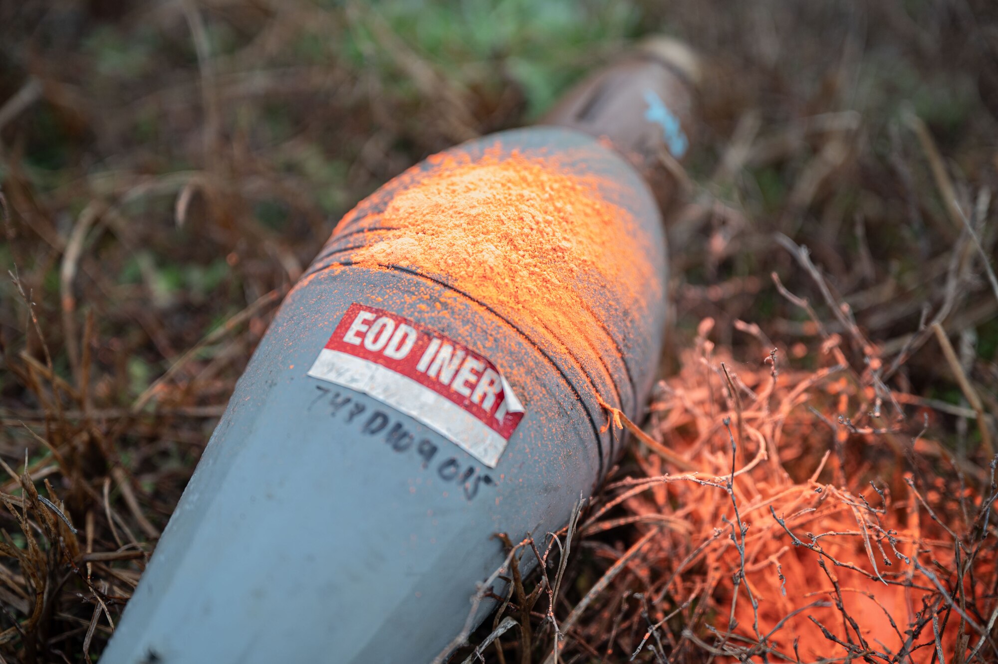 A training munition sits on the ground with orange marking chalk on it.