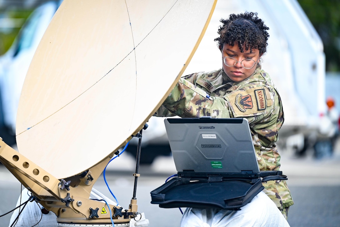 An airman looks at her laptop as she works on a satellite dish.