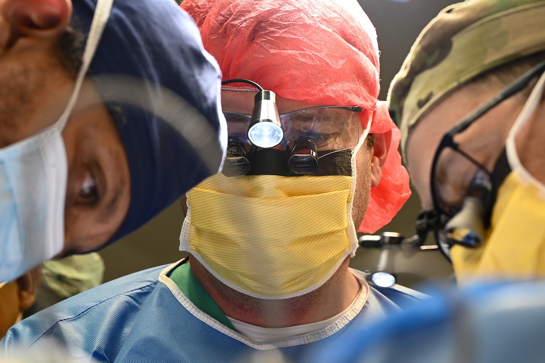 Close-up of three medical professionals in scrubs, two wearing glasses and headlights, looking down.