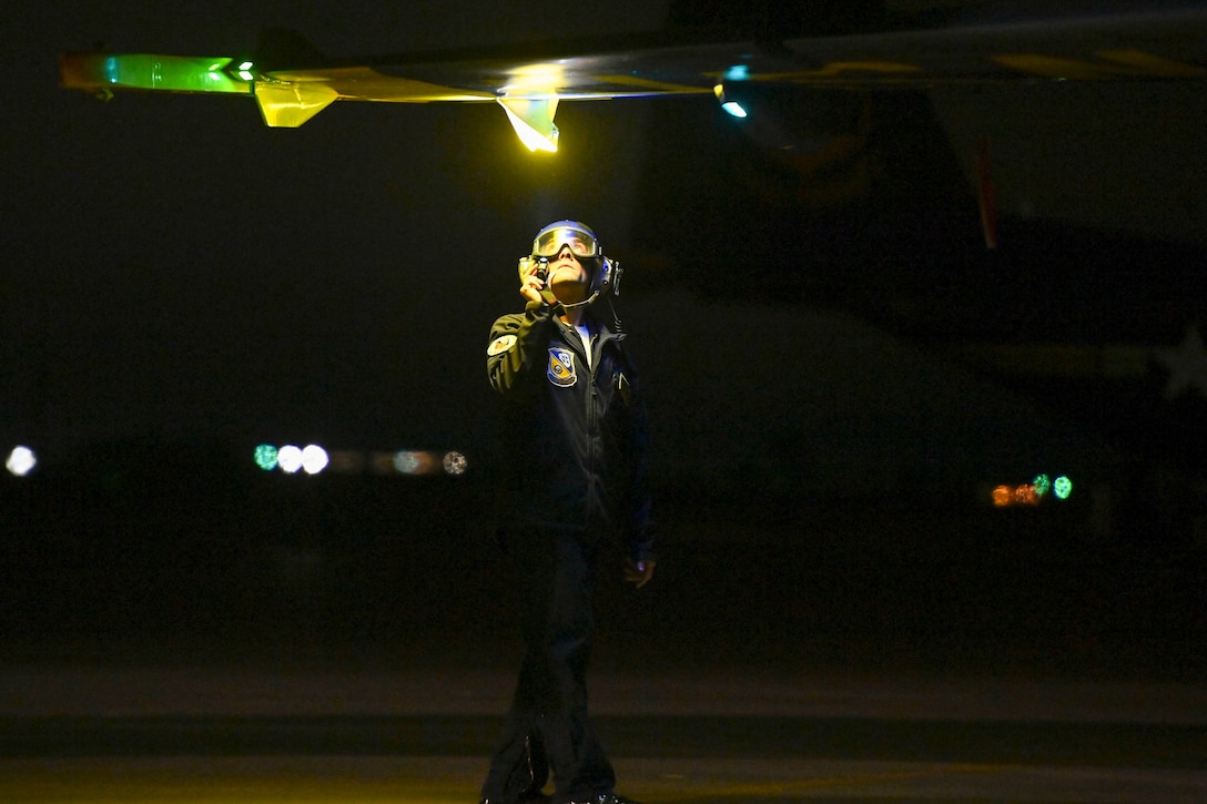 A service member standing in the dark shines a light on the wing of an aircraft.