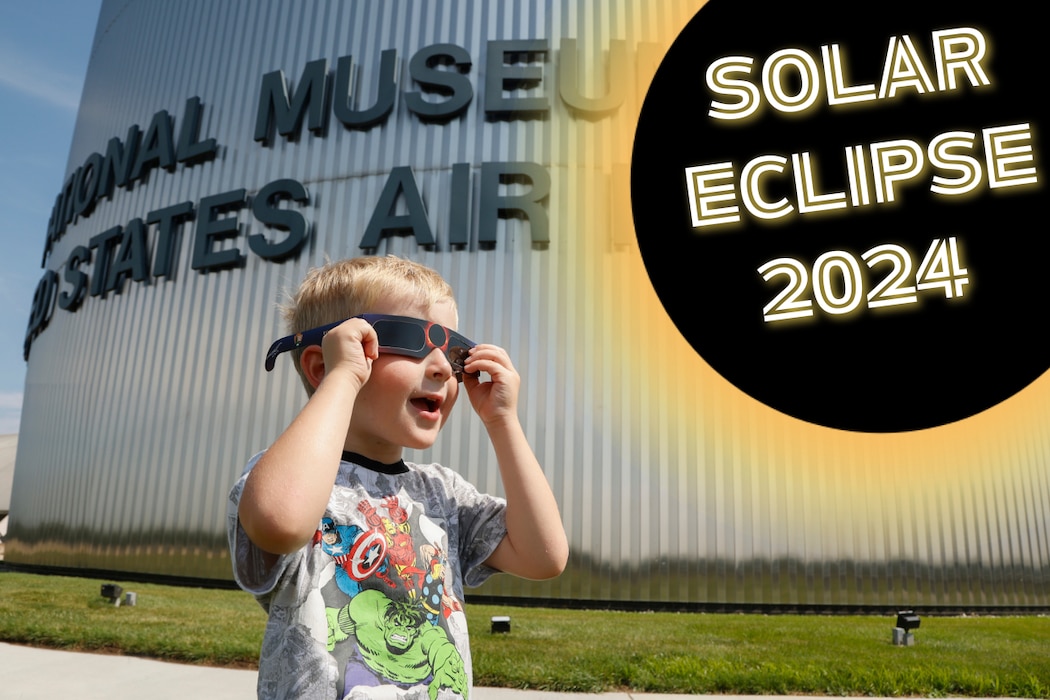 Solar Eclipse 2024. Imageof a boy wearing solar eclipse glasses while standing in front of the musem and looking up towards a graphic of an eclipse.