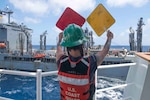 Petty Officer 2nd Class Mikayla Parnell relays signals on the fueling deck of U.S. Coast Guard Cutter Bertholf (WMSL 750) during a refueling at sea evolution with U.S. Naval Ship John Ericsson (T-AO 194) on Feb. 23, 2024, in the South China Sea. Bertholf is deployed to the Indo-Pacific region to advance relationships with ally and partner nations. (U.S. Navy photo by Mass Communication Specialist 3rd Class Charlotte Duran)