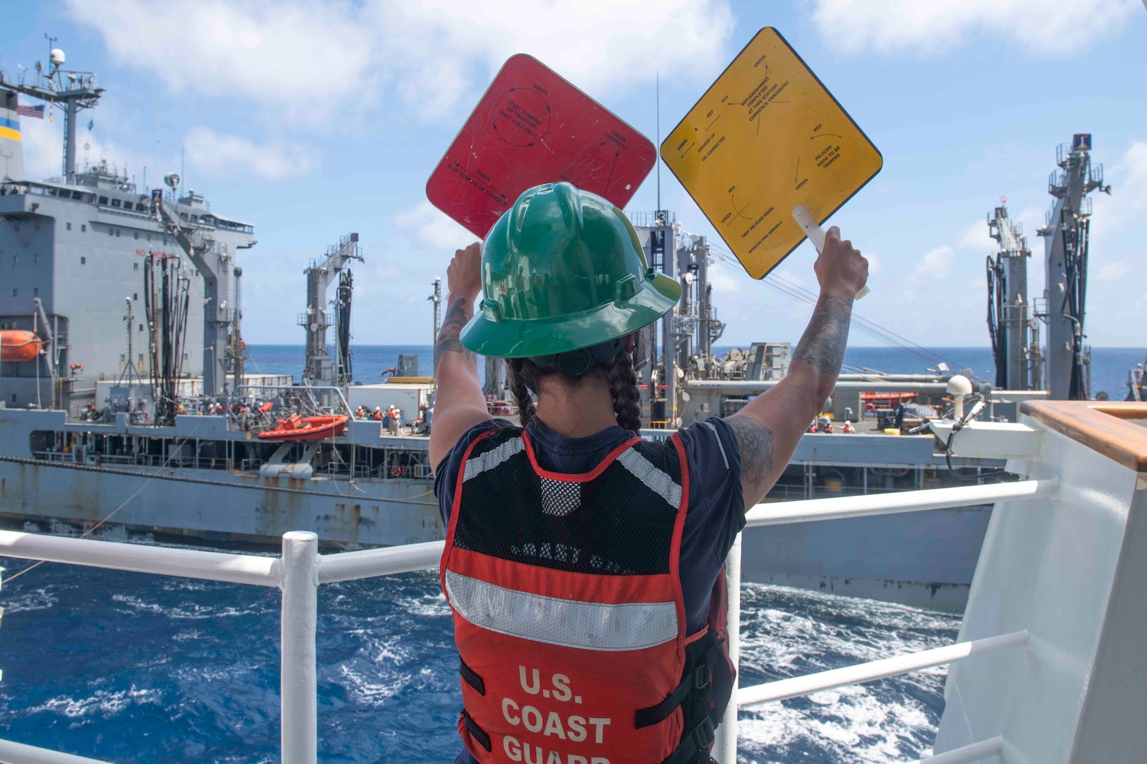 Petty Officer 2nd Class Mikayla Parnell relays signals on the fueling deck of U.S. Coast Guard Cutter Bertholf (WMSL 750) during a refueling at sea evolution with U.S. Naval Ship John Ericsson (T-AO 194) on Feb. 23, 2024, in the South China Sea. Bertholf is deployed to the Indo-Pacific region to advance relationships with ally and partner nations. (U.S. Navy photo by Mass Communication Specialist 3rd Class Charlotte Duran)