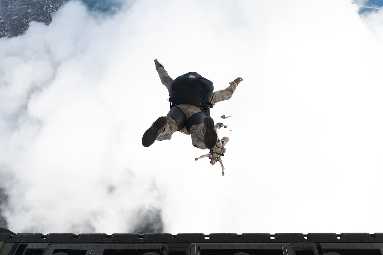 Service members jump out of an aircraft.