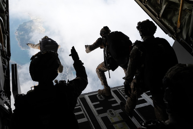 Service members jump out of an aircraft.