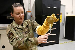 Senior Airman Stephanie Gillispie, 445th Maintenance Squadron non-destructive inspector, explains how to measure magnetic particles used in an oil bath under normal lighting, Feb. 4, 2024.