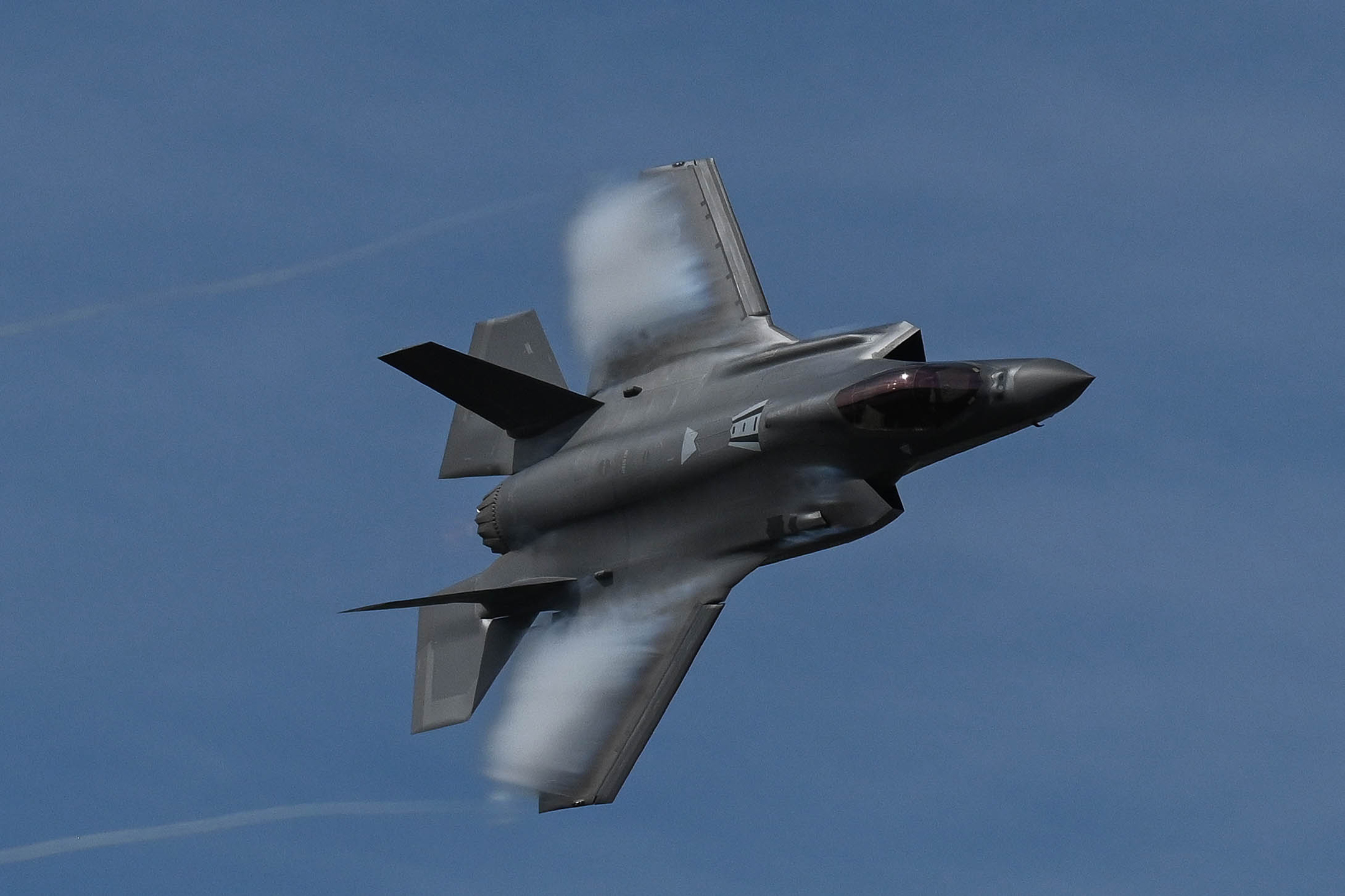 A military fighter aircraft flies against a blue sky. 