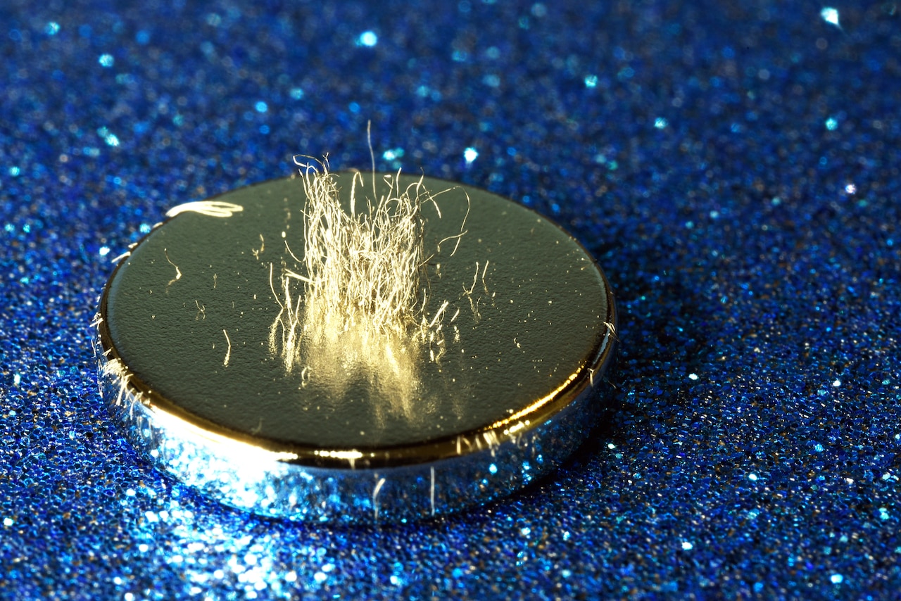 A silvery metal disc sits atop a sparkly blue surface. Metal shavings stand on edge.