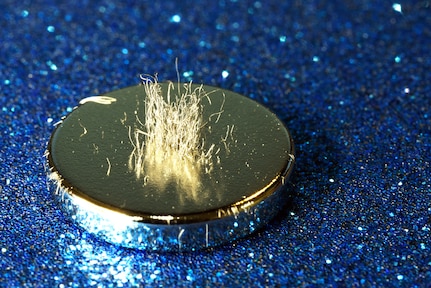 A silvery metal disc sits atop a sparkly blue surface. Metal shavings stand on edge.