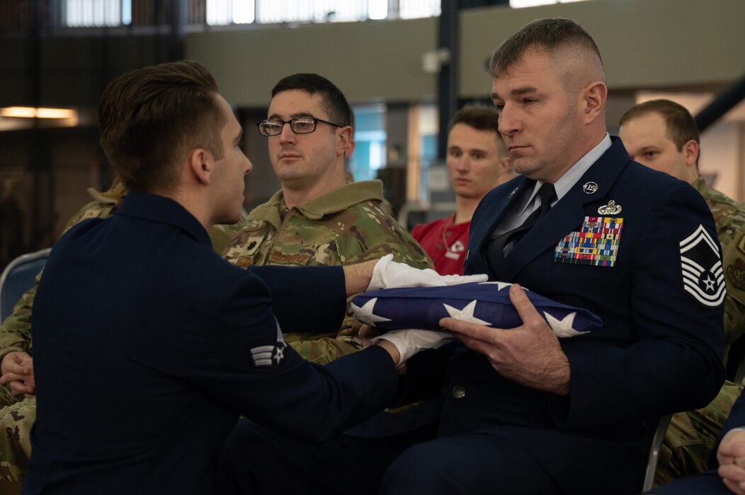 U.S. Air Force Senior Airman Jonas Ybarra presents a folded American flag to a senior enlisted leader during a full honors funeral demonstration.