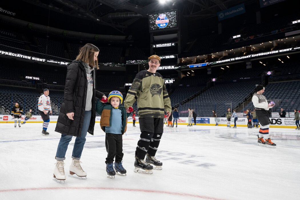 A man and woman hold a young boy's hands while ice skating.