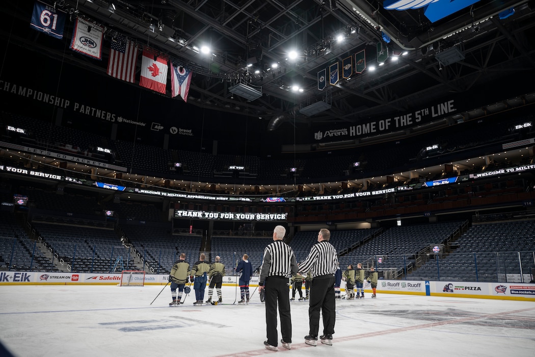 Two referees and a team of hockey players in green jerseys stand on an ice rink during the national anthem.