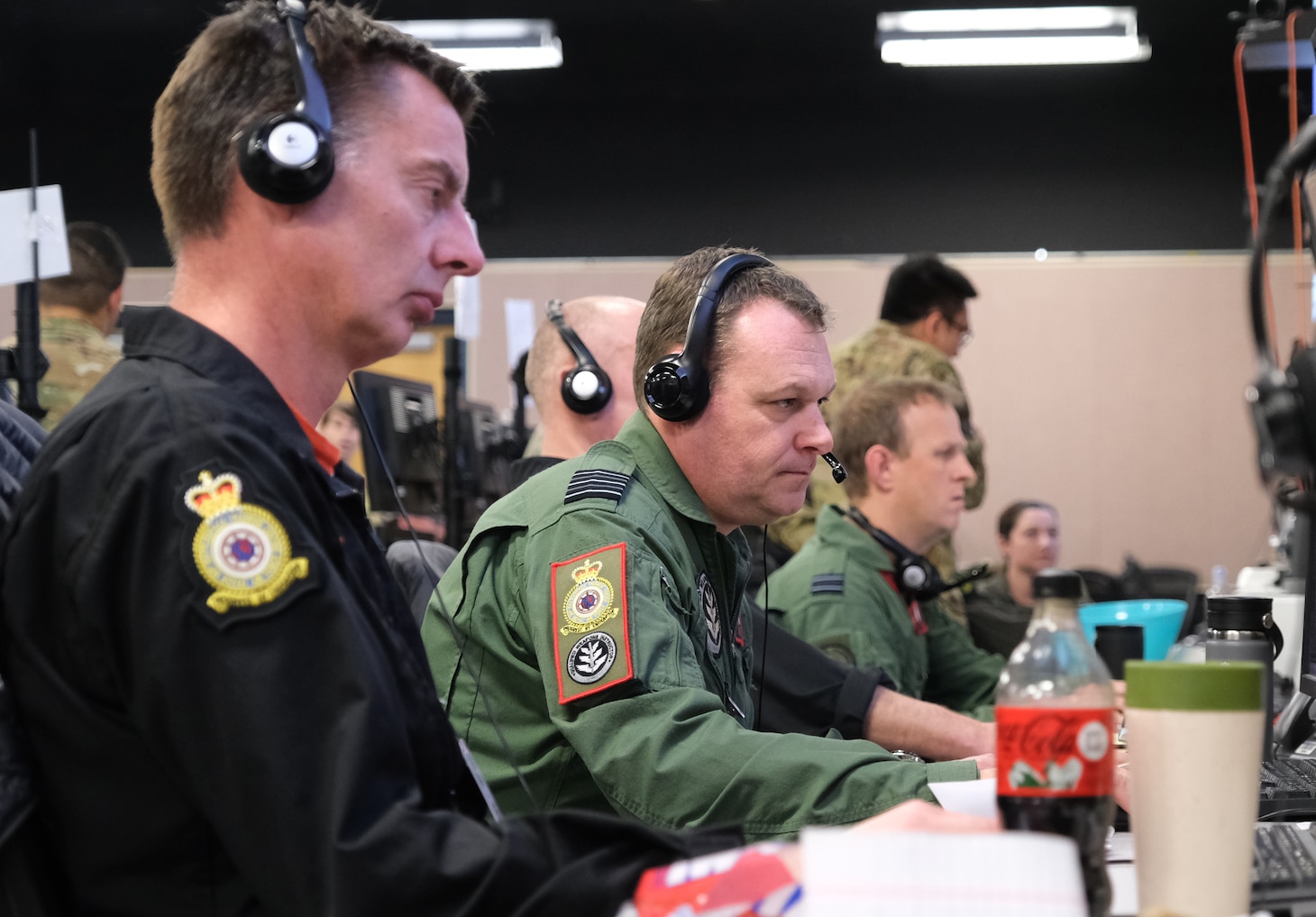 uniformed coalition forces wearing headsets, work at computers