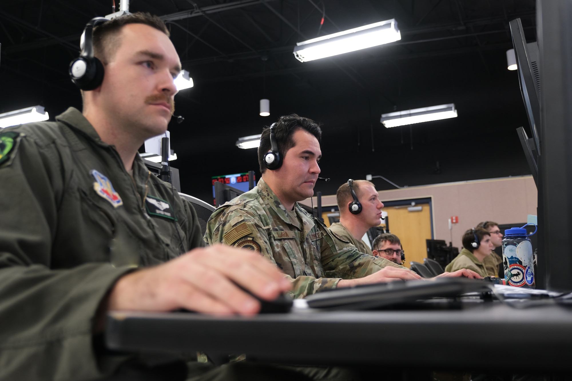 uniformed U.S. Air Force Airmen wearing headsets work at computers