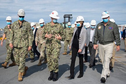 Uniformed service members walk alongside civilians while talking.