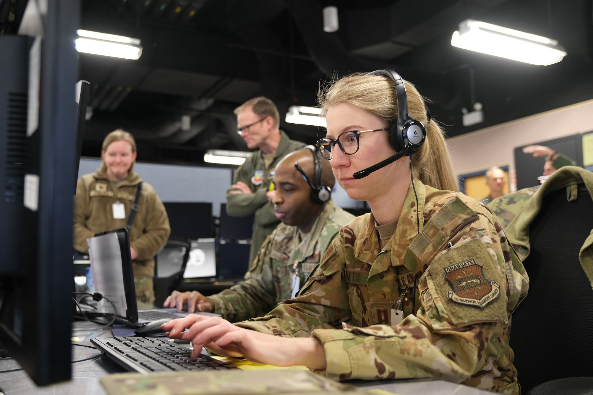 uniformed U.S. Air Force Airmen work at computers in the background are multiple computer screens