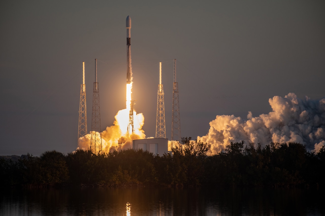 A rocket launches at night leaving a trail of smoke.