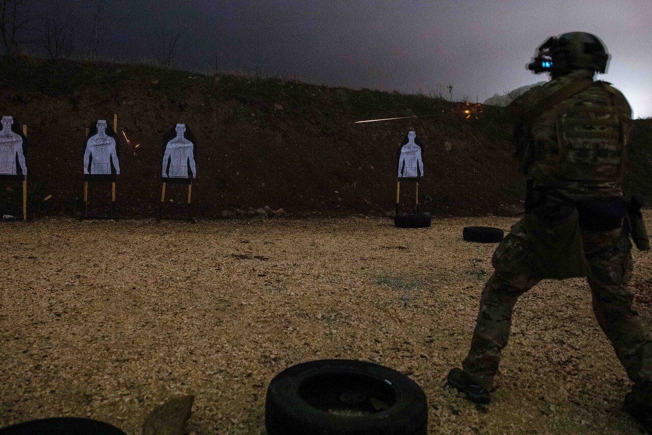 A soldier fires at a target in a darkened area.