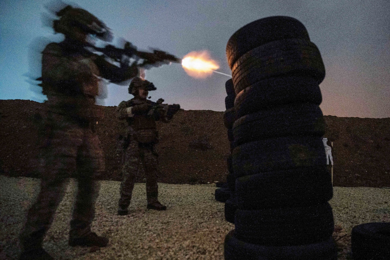 A soldier fires a weapon at a stack of tires.